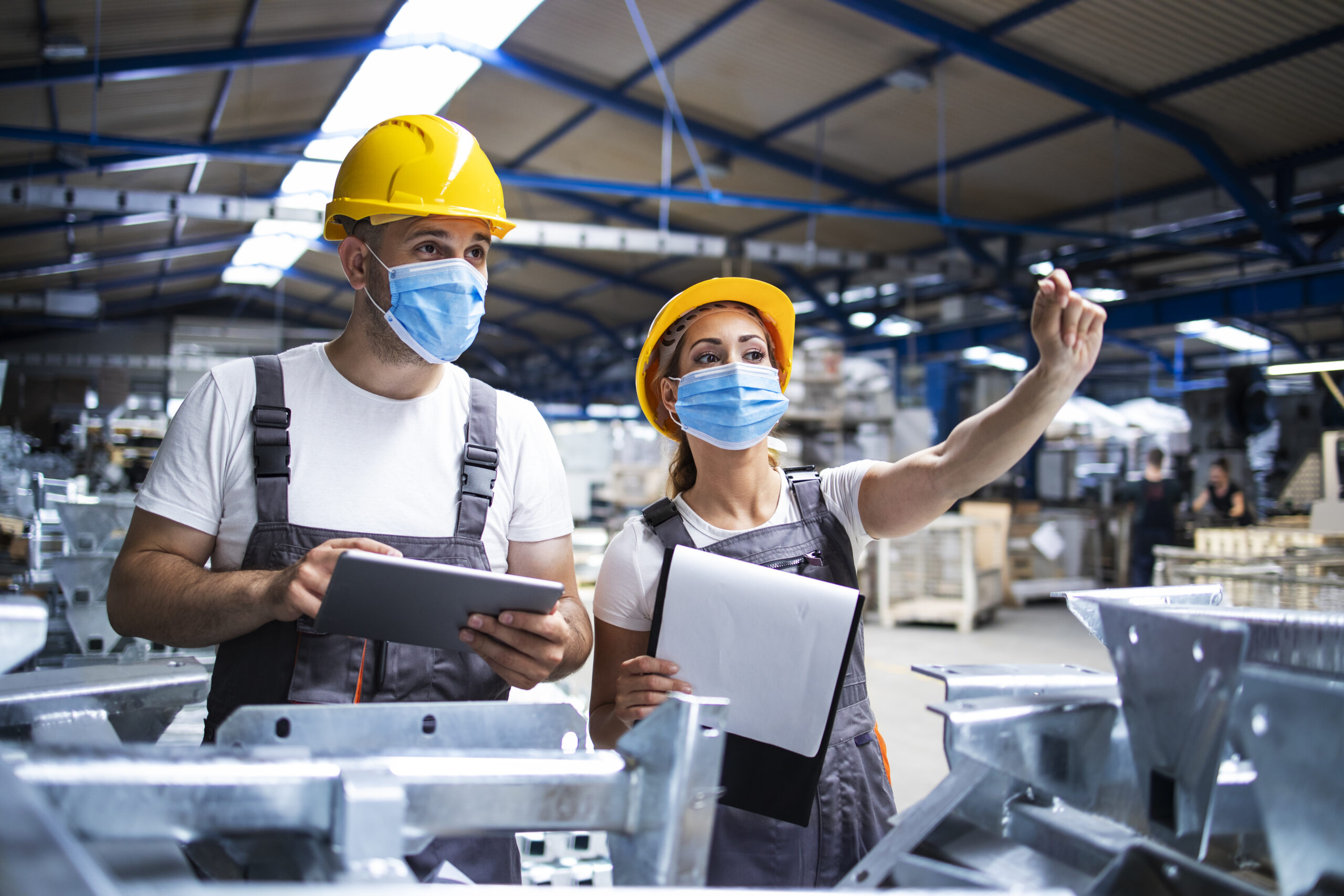 factory workers with face masks protected against corona virus doing quality control of production in factory scaled